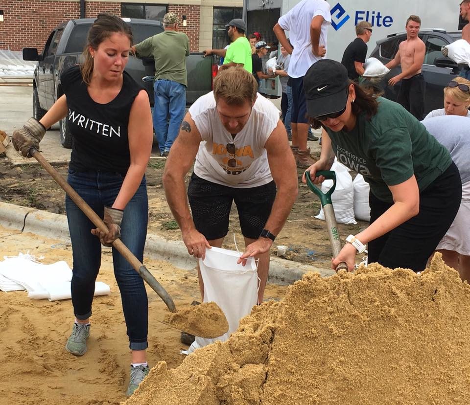 3 people work together to shovel sand from an enormous pile into sandbags during the 2016 Cedar Rapids flood