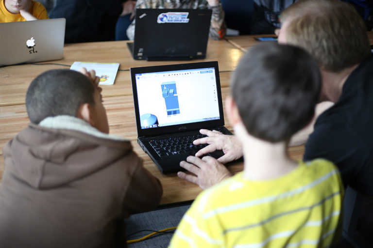 A CoderDojo facilitator demonstrates 3-D modeling for 2 students on a laptop