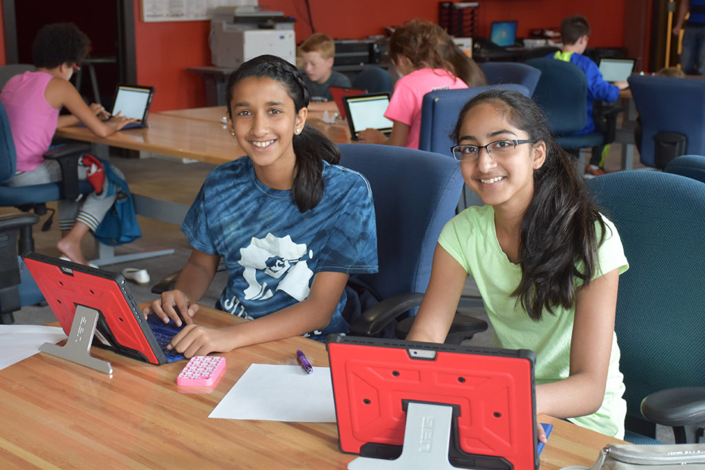 2 Code++ participants smiling at the camera as they learn to code on sponsor-provided tablets