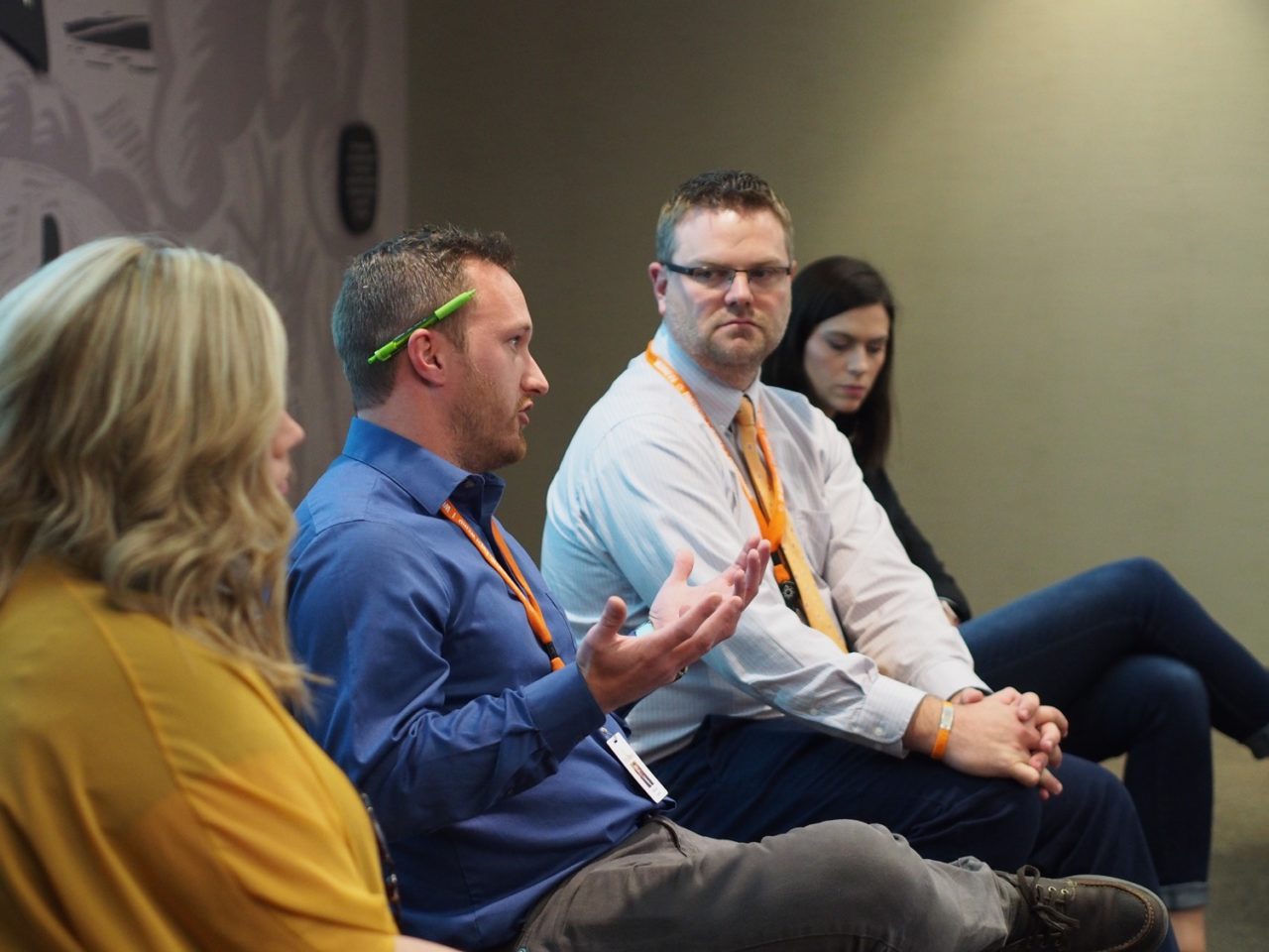 Three Intrapreneur Academy attendees in business attire listen attentively to a fourth, who gesticulates while explaining themselves