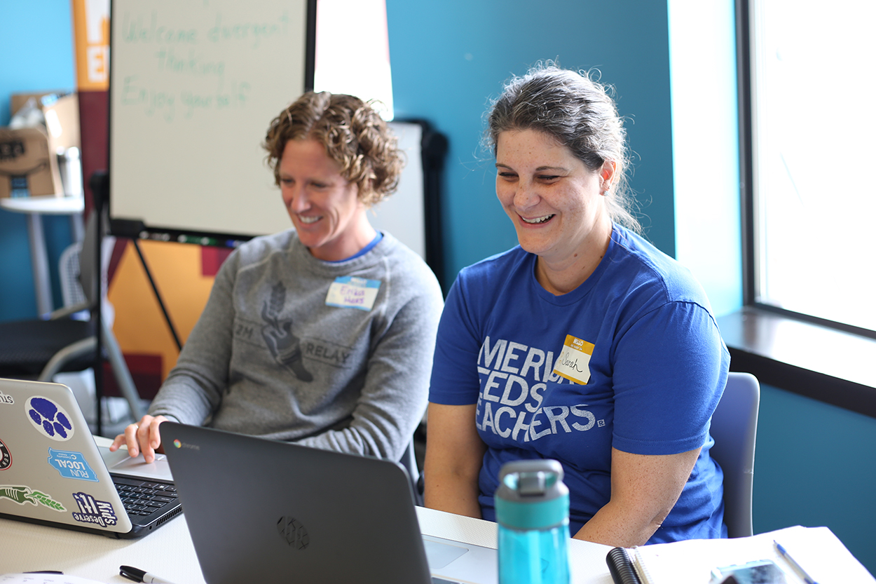 Two teachers smiling and laughing as they learn about tech education at their laptops