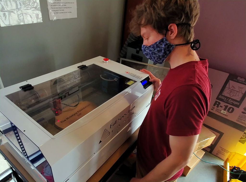A NewBoCo employee working with a Full Spectrum Laser cutter to produce an engraved plaque for The McIntyre Foundation, a sponsor organization