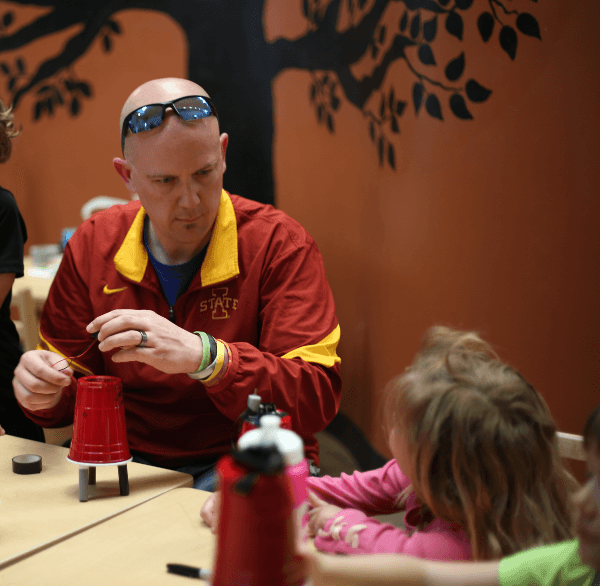 NewBoCo Executive Director, Aaron Horn, aides children in assembling a robotics project using a plastic cup and markers