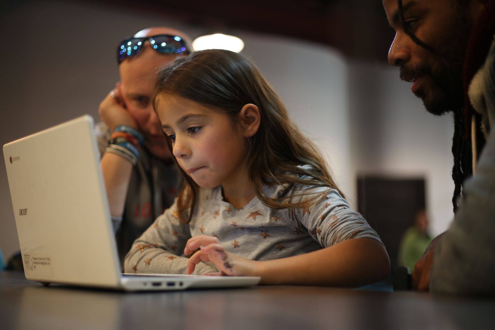 A young CoderDojo participant and two volunteers gather around a laptop to work through a code challenge at one of the stations.
