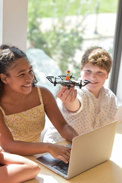 Two CoderDojo students gleefully learn while they play with a remote-controlled drone