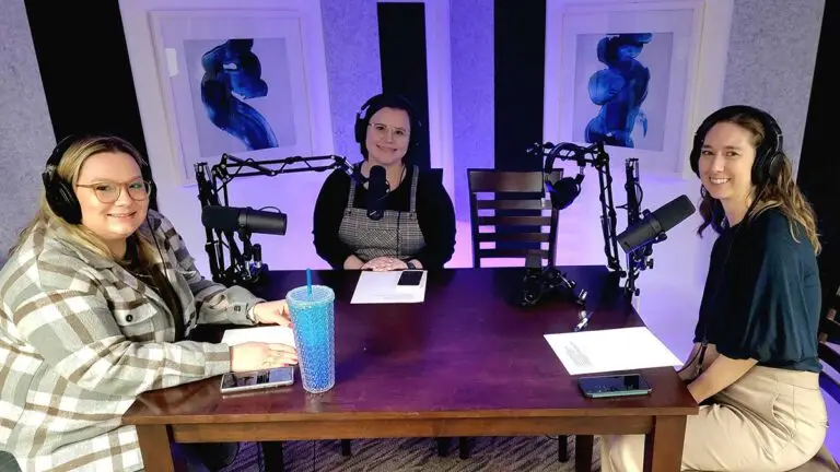 3 Iowa Innovation podcast hosts smile at the viewer as they sit at a table with microphones in front of them