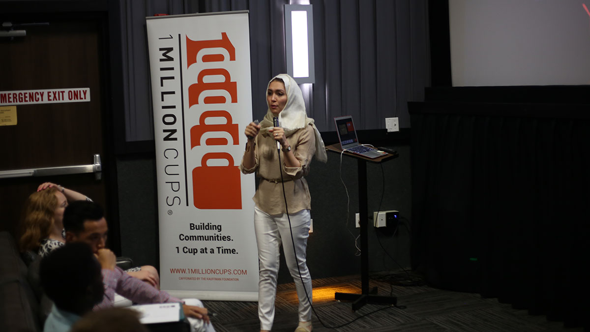 A presenter motions with her hands as she explains a concept to a 1 Million Cups audience