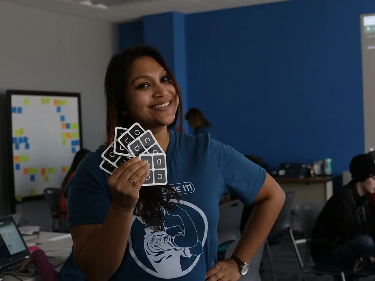 A smiling person stands, hand on hip, and holds up a fanned series of cards with "C-O-D-E" on them