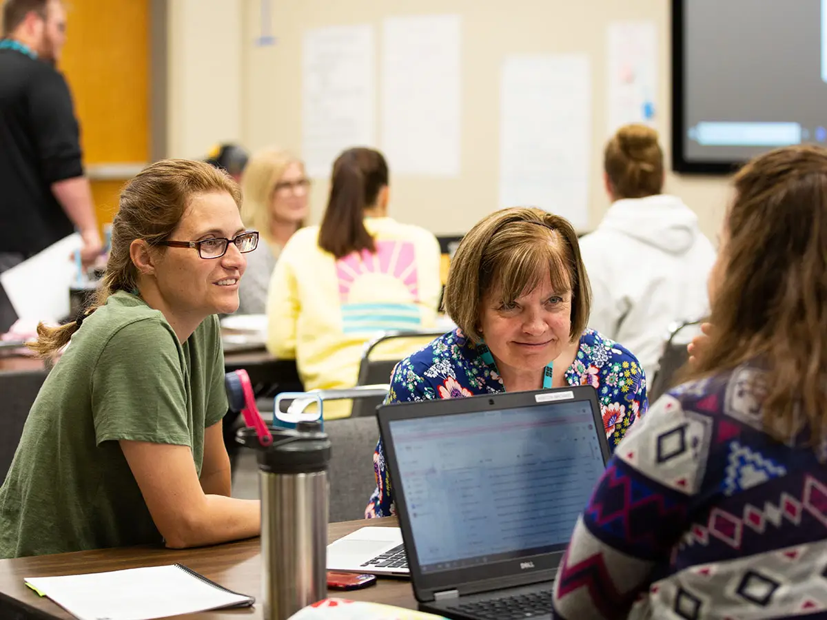 2 Code.org teachers lean in and smile as they listen to the input of a third teacher