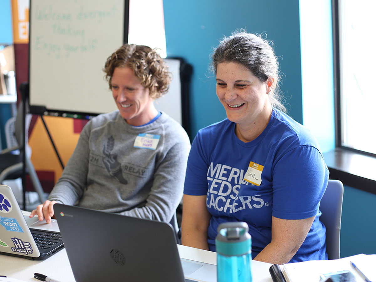2 teachers smile and laugh as they learn about tech education at their laptops