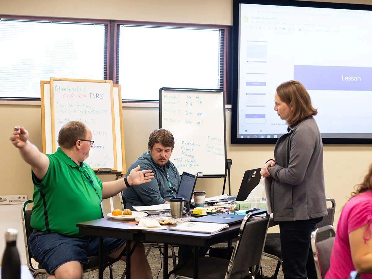 A teacher gestures to 2 other group members as they discuss a collaborative project