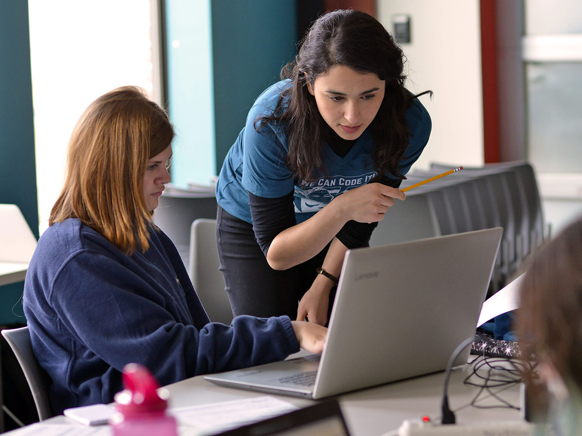 A volunteer guides a young student through a project on her laptop during Girls Who Code