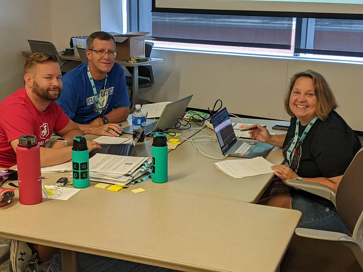 A group of 3 Code.org workshop participants pause their work to smile from around a table