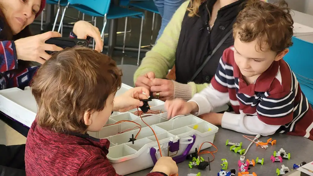 2 children play with a circuit project at CoderDojo while a parent takes a picture with their cell phone