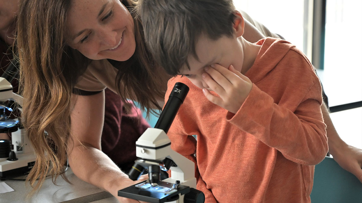 A mother helps her child look through a microscope during a CoderDojo event