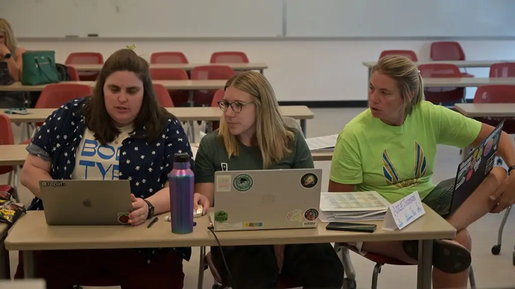 3 Project GUTS participants sit in a row and look to one participants computer they speak