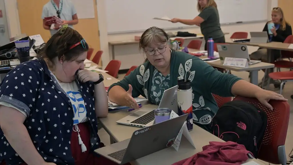 2 Project GUTS participants work through a project together; 1 gestures to their computer screen for the second