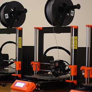 Plastic filament-fed 3D printers lined up in a row.
