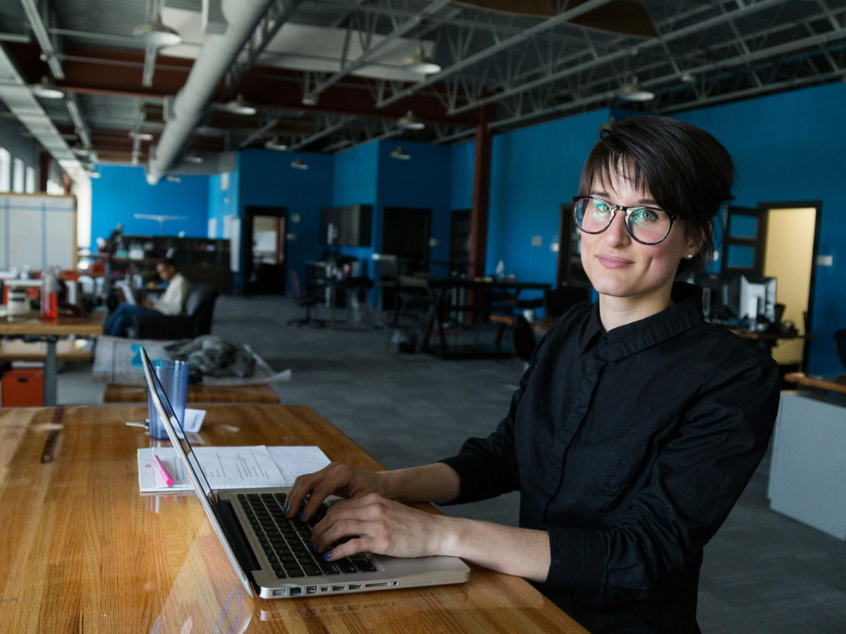 A Vault Coworking member poses and smiles at their desk with a laptop