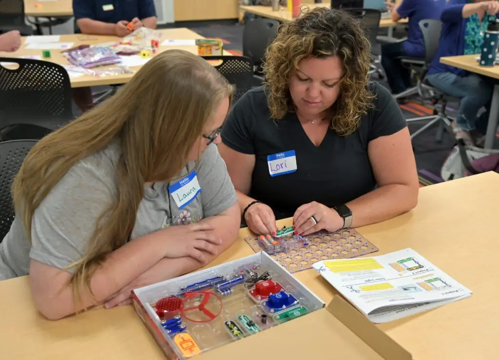 two teachers sitting at a desk, both closely learning about snap circuits.
