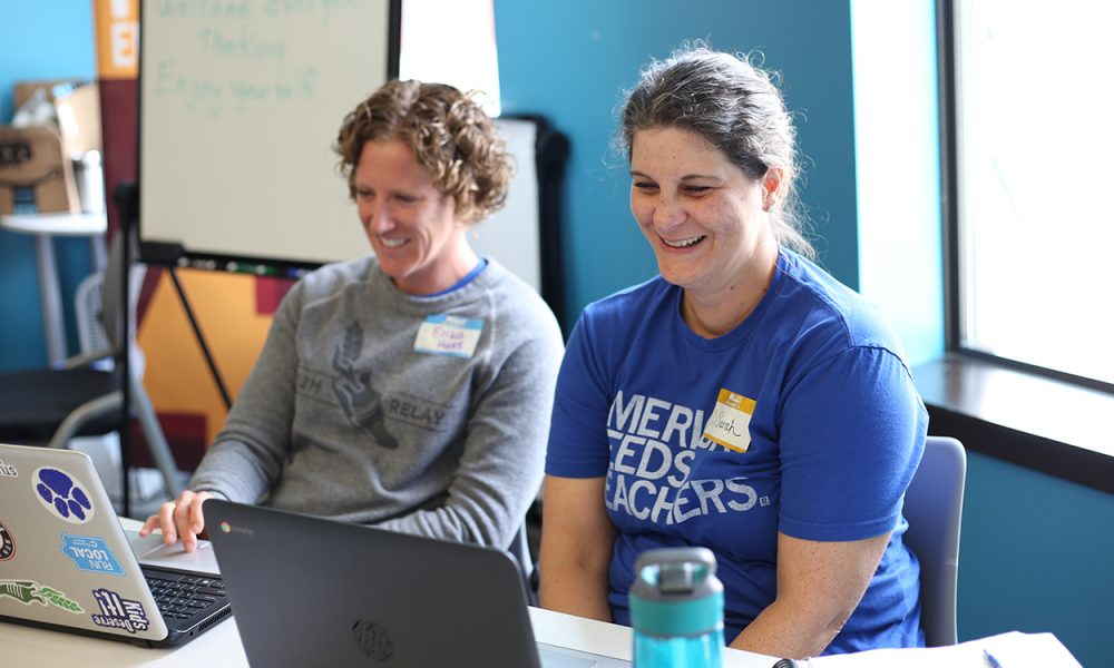 Two teachers smiling and laughing as they learn about tech education at their laptops