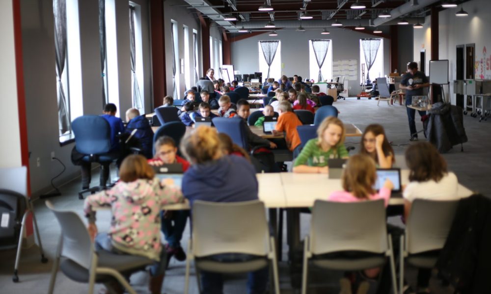 A NewBoCo conference room filled with kids and parents at round tables during a CoderDojo event