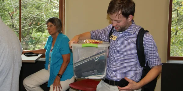 A Code.org facilitator laughs as he looks down at a tote full of classroom supplies that he carries