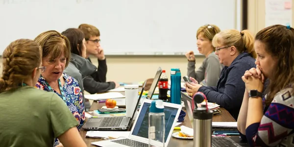 7 Code.org teachers sit together at a table; they are conversing as 2 different groups
