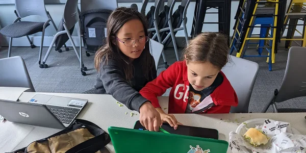 A young Girls Who Code Club participant points at her classmates laptop screen to help her